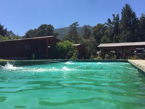 una piscina de agua verde frente a una casa en Cabañas Las Bandurrias del Caburgua, en Pucón