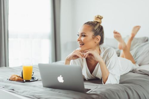 a woman laying on a bed with a laptop at LUST PREMIUM Apartments in Kragujevac