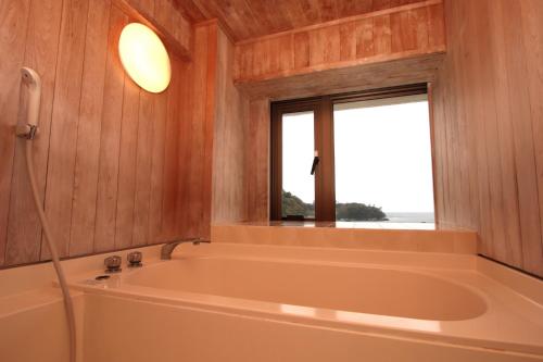 eine Badewanne in einem Zimmer mit Fenster in der Unterkunft Ooedo Onsen Monogatari Toi Marine Hotel in Izu