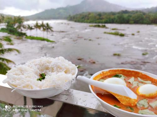 a bowl of noodles and a bowl of rice next to a river at The Anchorage Athirapilly Resort in Athirappally
