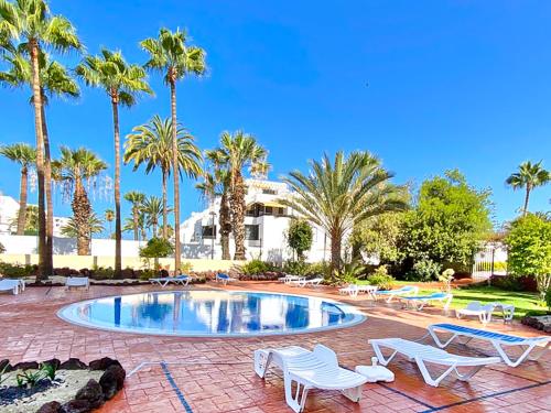 una piscina con sillas blancas y palmeras en El Dorado, en Playa de las Américas