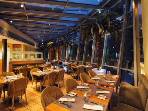 a restaurant with tables and chairs and palm trees at Mövenpick Hotel München-Airport in Hallbergmoos