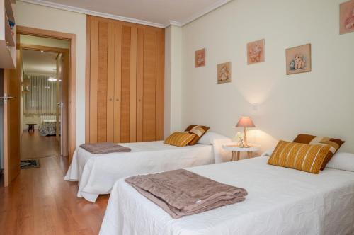 two beds in a room with white walls and wooden floors at Piso Turístico Perotas in Arévalo