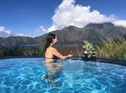 a woman in a swimming pool with a cat in the water at Batur Volcano Guesthouse in Kintamani