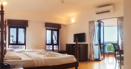 a bedroom with two beds and a television and windows at Hotel Arcadia in Panaji