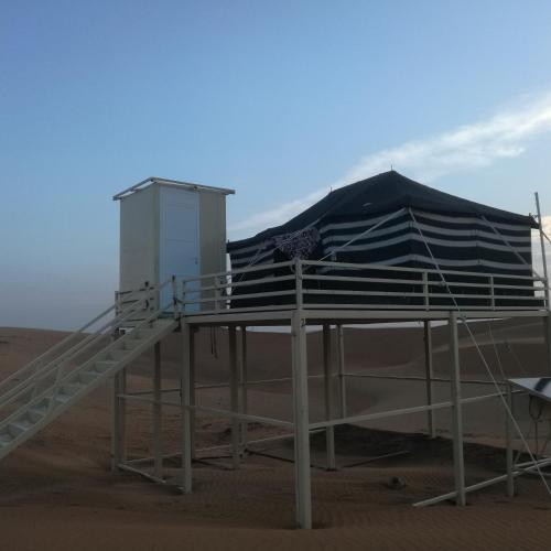 a beach shelter with an umbrella in the sand at Oman desert private camp in Shāhiq