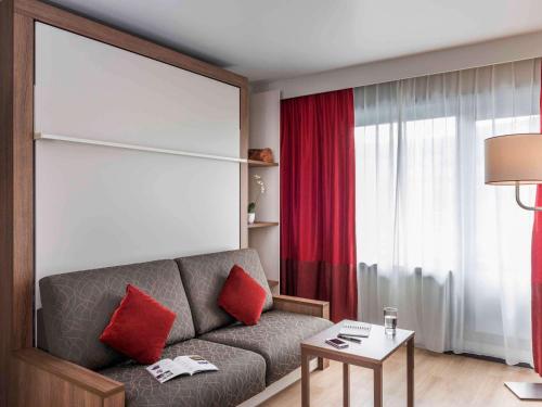 - un salon avec un canapé gris et des oreillers rouges dans l'établissement Aparthotel Adagio Paris Bercy Village, à Paris