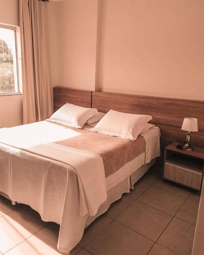 a bedroom with a bed with white sheets and a window at Hotel Monte Carlo in São João del Rei