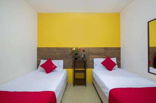 two beds in a room with yellow walls and red pillows at Hotel Villa Hermosa in Oaxaca City
