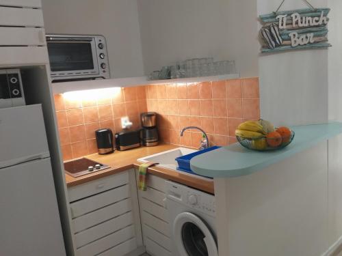 a kitchen with a washing machine and a bowl of fruit on a counter at MANGANAO LOFTS INN Bord de Mer in Saint-François