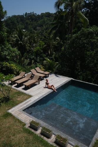a woman sitting in a swimming pool with lounge chairs at Good Vibes Villas in Unawatuna