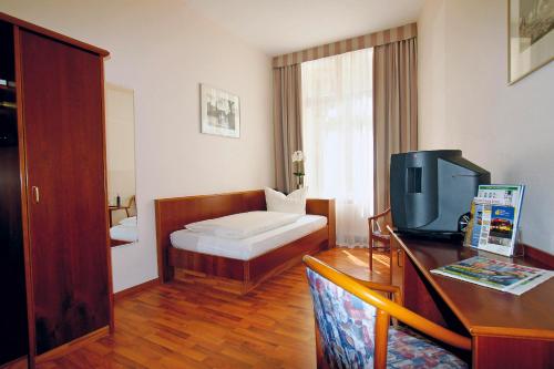 a room with a bed and a desk with a television at Hotel Deutsches Haus in Braunschweig