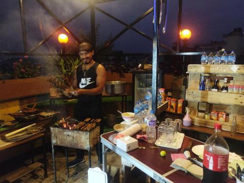 a man standing in a kitchen with a table with food at Yog Hostel- Rooftop Yoga & Backpacker Social Stay in Thamel, Kathamndu in Kathmandu