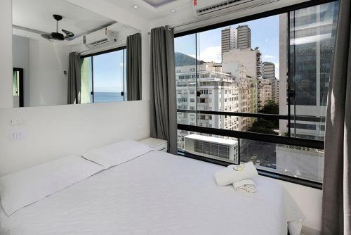 1 dormitorio con cama blanca y ventana grande en Studio moderno com vista privilegiada para a praia, en Río de Janeiro