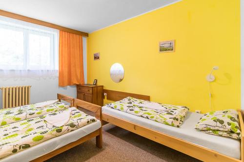two beds in a room with a yellow wall at Penzion Vápenka in Horní Maršov