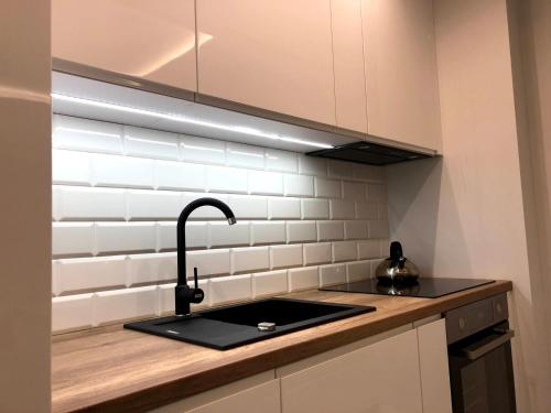 a kitchen with a black sink and white tiles at Downtown Apartment in Toruń