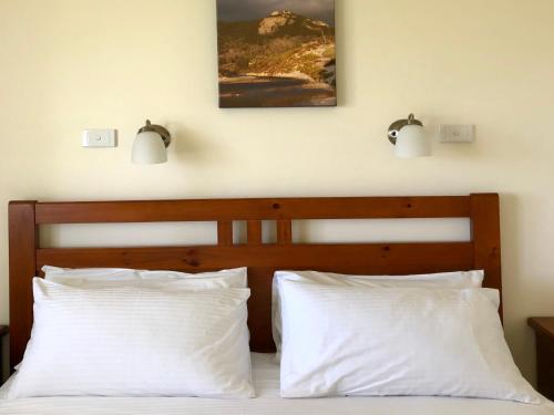 a bed with two white pillows and two lights on the wall at Promhills Cabins in Yanakie