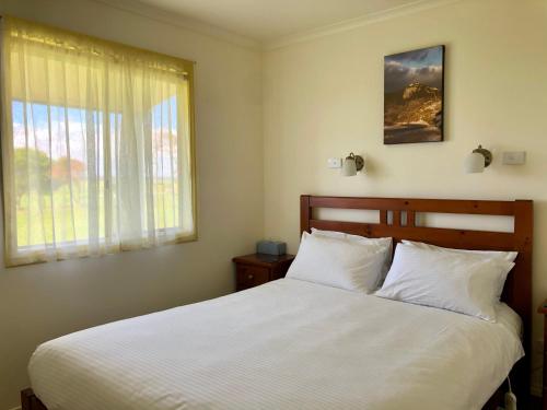 1 dormitorio con 1 cama blanca grande y ventana en Promhills Cabins, en Yanakie