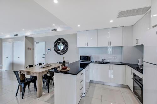 a kitchen with white cabinets and a table and chairs at Lakeside Waterfront Apartment The Entrance in The Entrance
