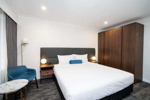 a bedroom with a white bed and a blue chair at Littomore Suites Bathurst in Bathurst