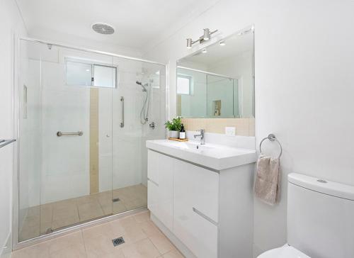 a white bathroom with a shower and a sink at kims@kiama in Kiama