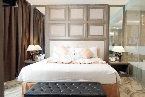 a bedroom with a large white bed with a black bench at Aston Lampung City Hotel in Bandar Lampung