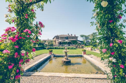 a garden with a fountain in front of a house with pink flowers at Capannelle Wine Resort in Gaiole in Chianti