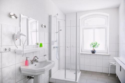 ein weißes Bad mit einer Dusche und einem Waschbecken in der Unterkunft Pension Bertha in Jena