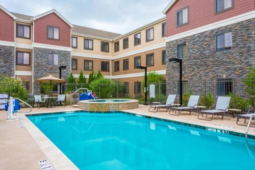 a swimming pool in a courtyard with chairs and a building at Staybridge Suites - Kansas City-Independence by IHG in Independence