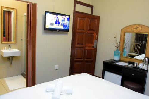 - une chambre avec un lit, un miroir et une télévision dans l'établissement Houghton Guest House, à Johannesbourg