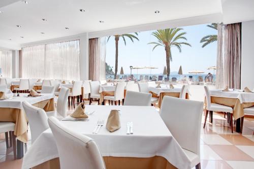 un restaurante con mesas y sillas blancas y palmeras en Grupotel Imperio Playa, en Sant Joan de Labritja