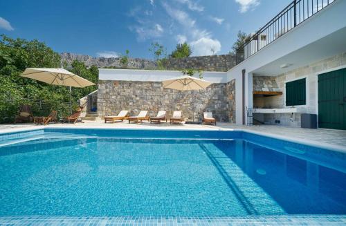 a pool with chairs and umbrellas next to a house at Luxury Residence Mladenka in Jesenice