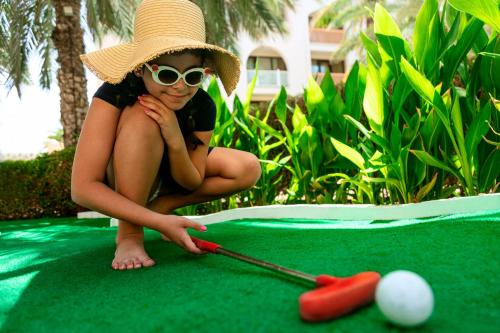 a woman in a hat and sunglasses playing pool at Shangri-La Barr Al Jissah, Muscat in Muscat