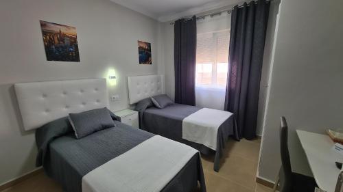 a small bedroom with two beds and a window at Hostal Málaga in Arcos de la Frontera