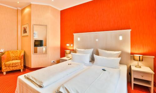 a bedroom with a large white bed with an orange wall at Hotel Stadt Kappeln in Kappeln