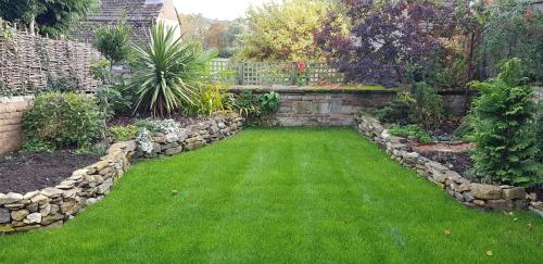 a garden with green grass and a stone wall at Meadow House in Stamford