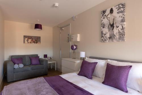 Isabella House - Hereford City Centre Aparthotel, By RentMyHouse في هيريفورد: غرفة نوم مع سرير مع وسائد أرجوانية وأريكة