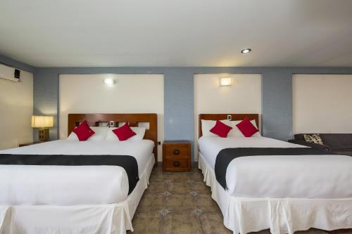 two beds in a hotel room with red pillows at Suites de Reyes in Irapuato