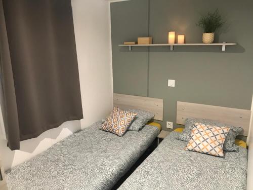 Cette chambre comprend 2 lits avec des oreillers et une étagère. dans l'établissement Mobil home au calme au Cap-Ferret - Camping les viviers "au bord du bassin", à Lège-Cap-Ferret
