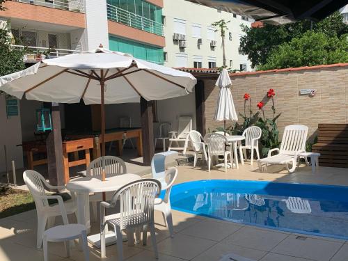 una mesa con sillas y una sombrilla junto a la piscina en Beach House Floripa, en Florianópolis