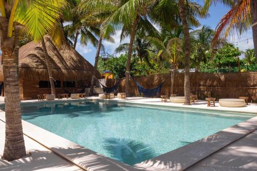 a swimming pool with palm trees and a hut at Selina Poc Na Isla Mujeres in Isla Mujeres