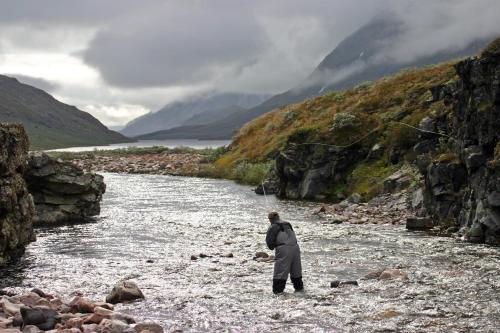 a man is standing in a river in the mountains at Igdlo Guesthouse in Narsaq