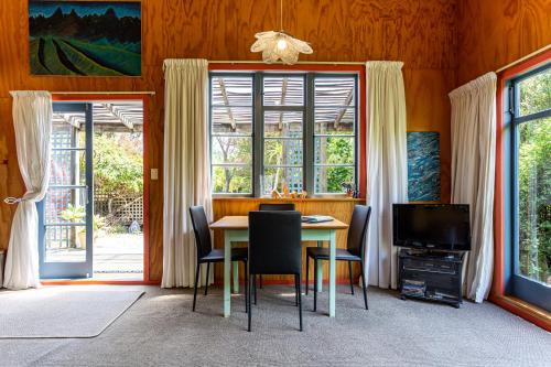 uma sala de jantar com mesa, cadeiras e janelas em Corru Gate em Mapua