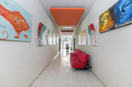 a corridor with a red couch in a hallway with paintings at Cityzen Renon Hotel in Denpasar