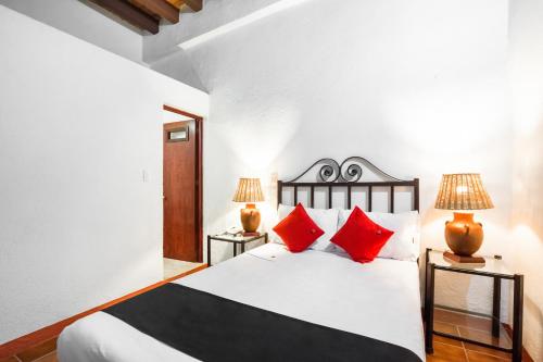 1 dormitorio con 1 cama blanca grande con almohadas rojas en Hotel El Nito Posada, en Oaxaca City