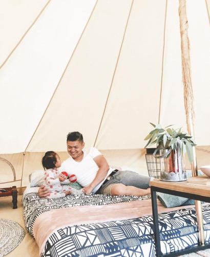 a man and a child sitting on a bed in a tent at Iluka Retreat Glamping Village & Group Lodge Accommodation in Red Hill South