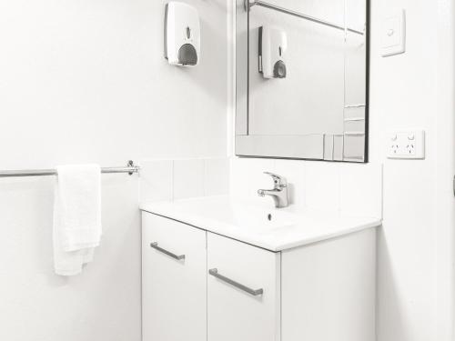 Baño blanco con lavabo y espejo en Cool Palms Motel, en Mackay