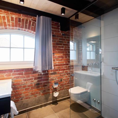 a bathroom with a toilet and a brick wall at meinwolfsburg hotel auf dem rittergut vormals Yard Boarding Hotel in Wolfsburg