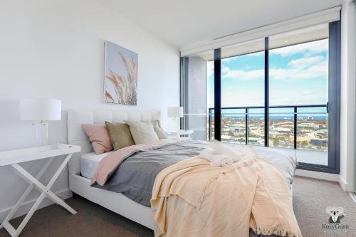 - une chambre blanche avec un lit et une grande fenêtre dans l'établissement KOZYGURU DOCKLANDS LUXURY WATER VIEW APT 1 BED VDO915, à Melbourne