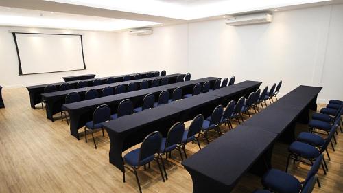 a conference room with black tables and chairs and a screen at Holiday Inn Fortaleza by IHG in Fortaleza